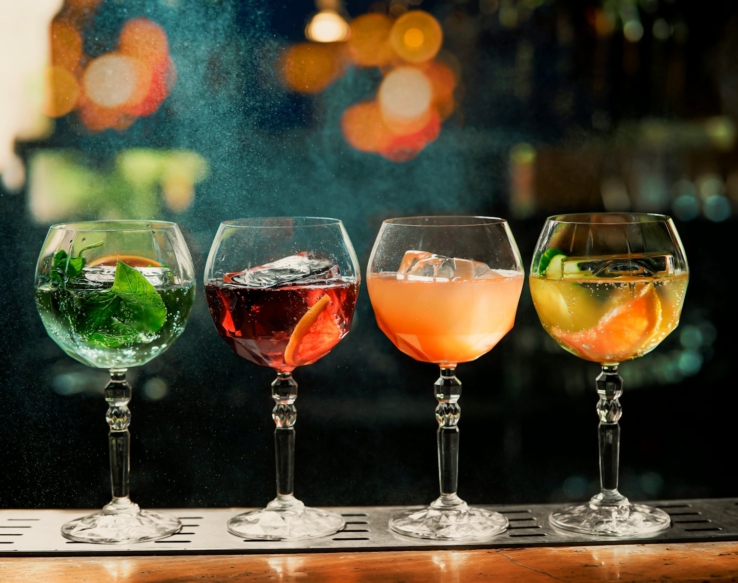 Quattro cocktail colorati su un bancone di legno lucido.