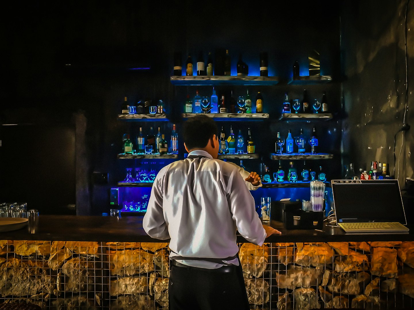 Un barista prepara cocktail dietro un bancone illuminato.