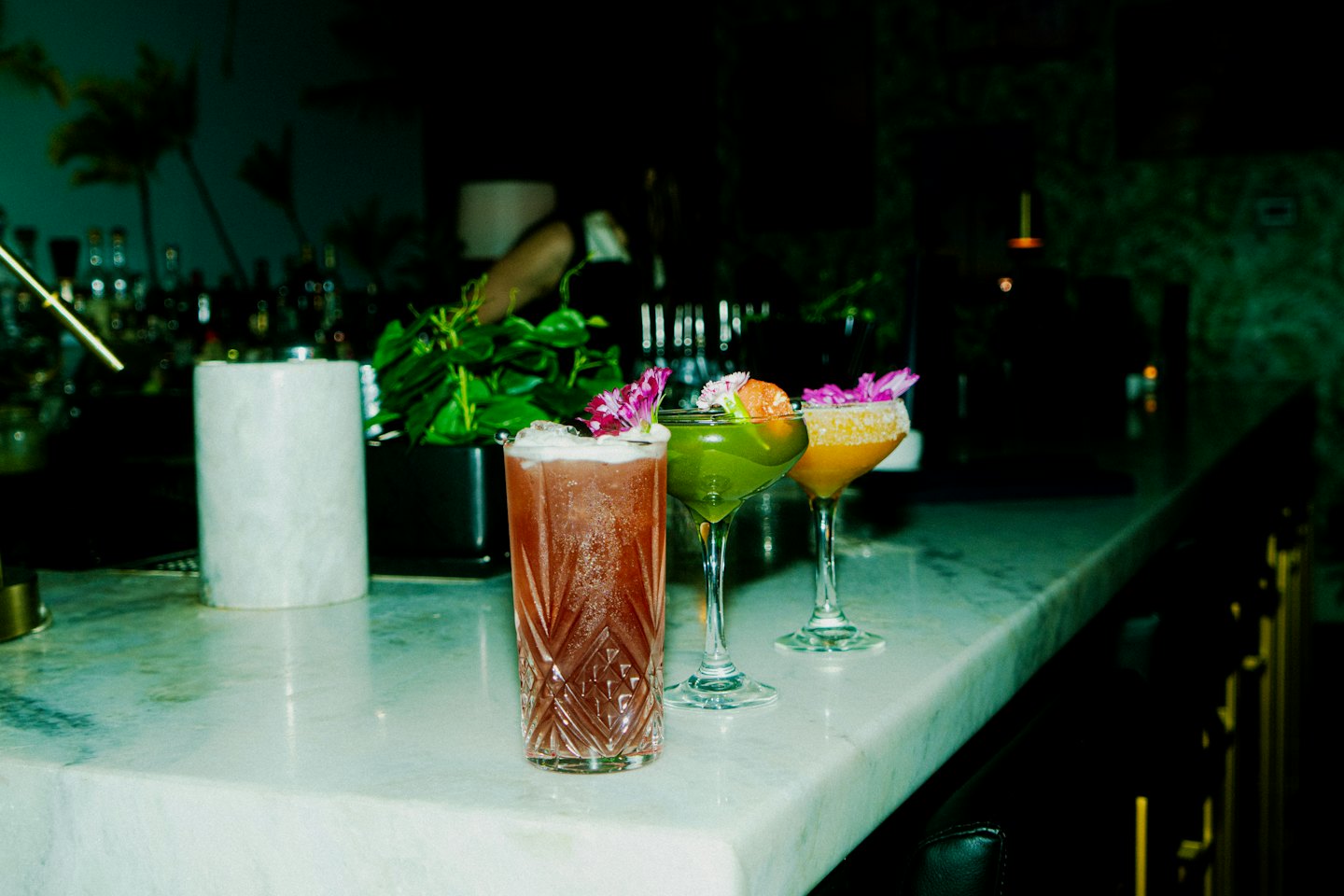 Tre cocktail colorati su un bancone di marmo.