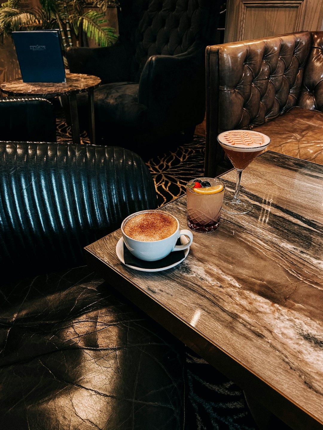 Due cocktail e un cappuccino su un tavolo di marmo.