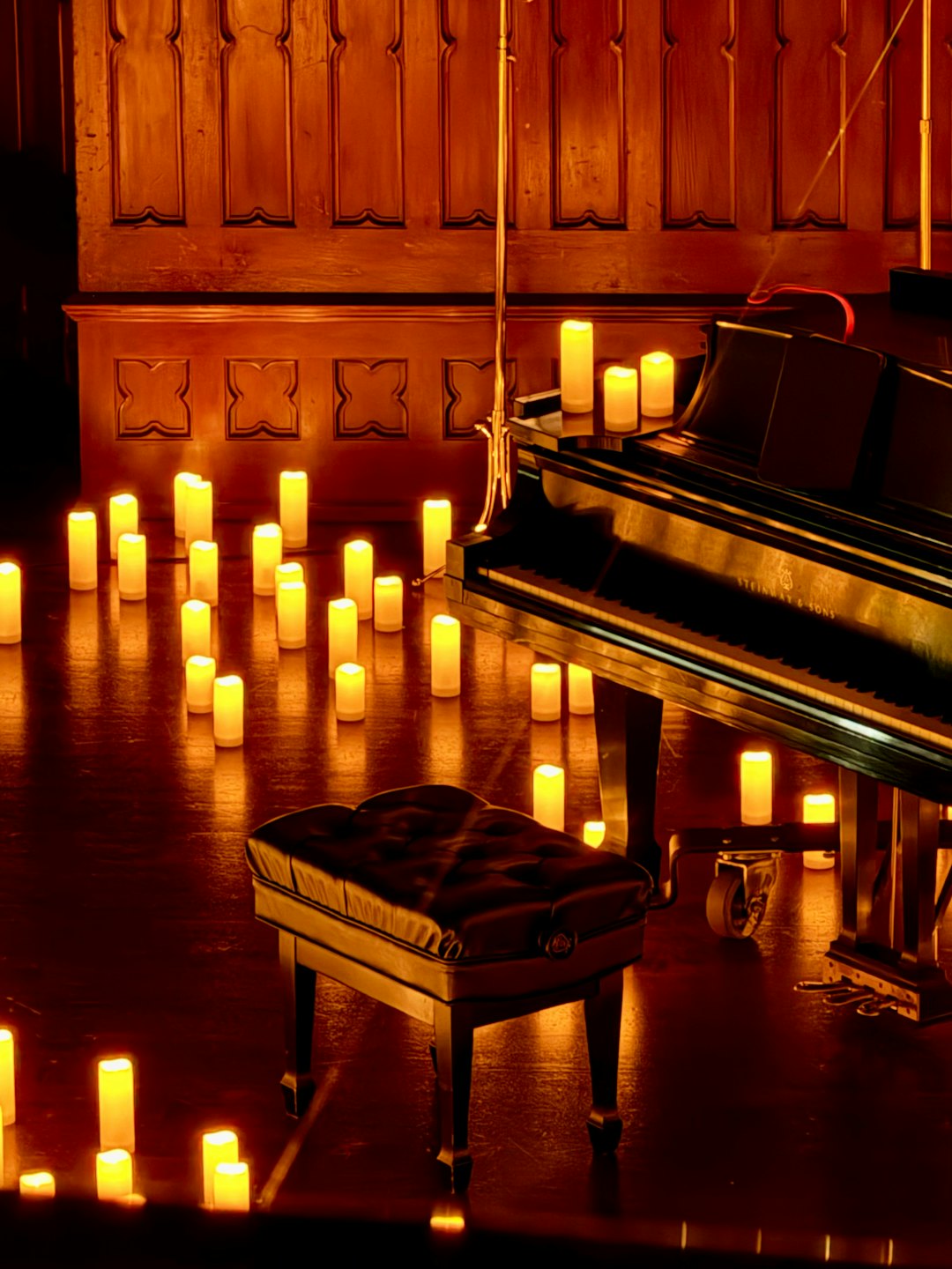 Un pianoforte a coda circondato da candele accese su un pavimento di legno.